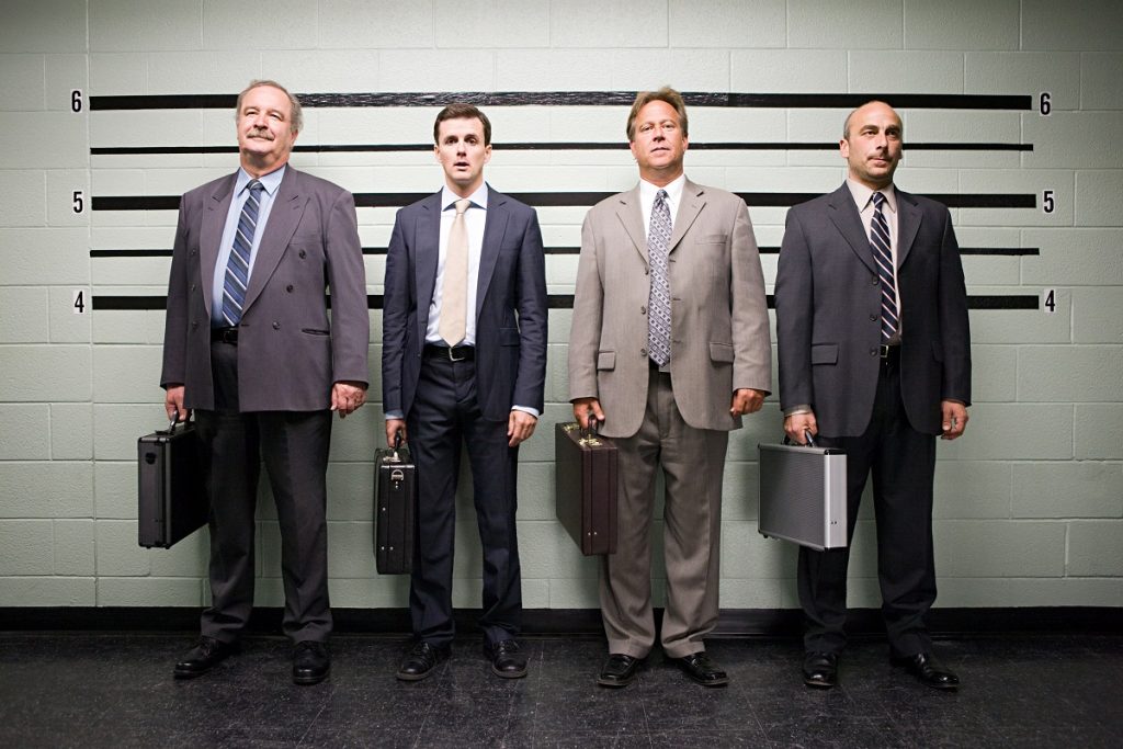 Four businessmen in suits are in a lineup with lines to show the height behind them.