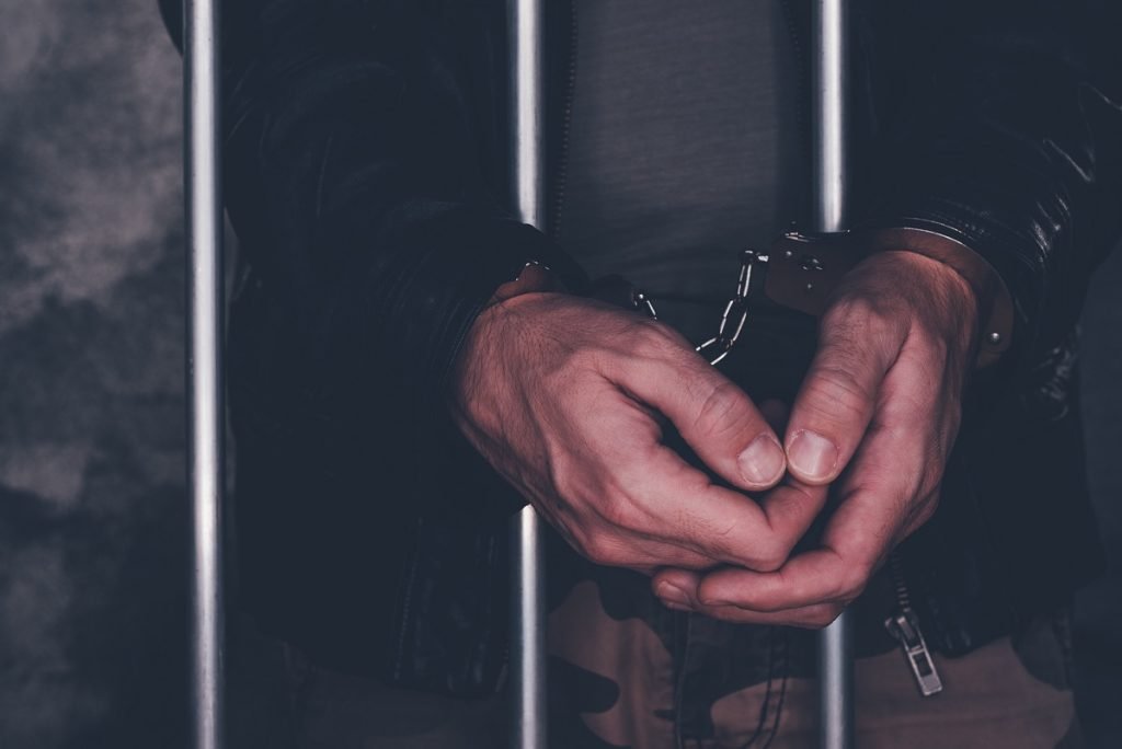 A pair of hands handcuffed to prison bars.