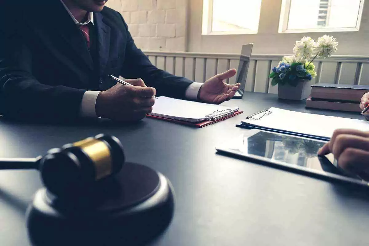 A lawyer and client sitting across from each other at a table with documents and a gavel.