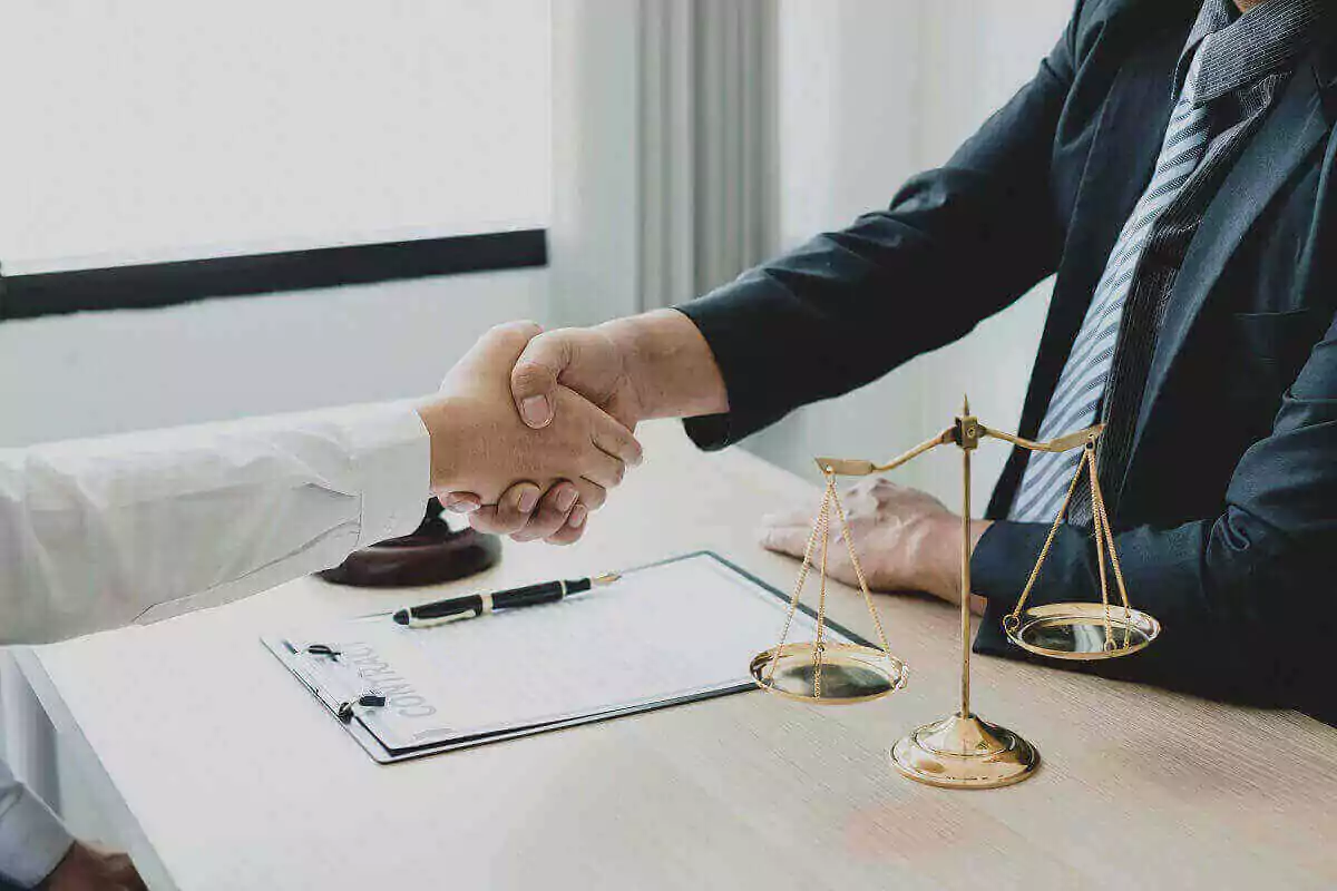 A lawyer shakes hands with his client across a desk with a set of scales.
