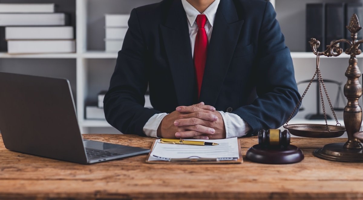 An attorney sitting at a desk with a laptop, scale, and gavel