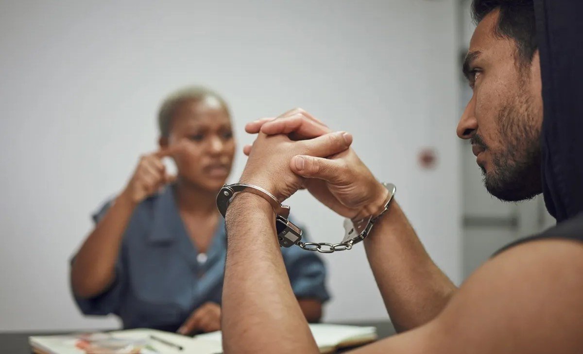 A man in cuffs being questioned by a police officer