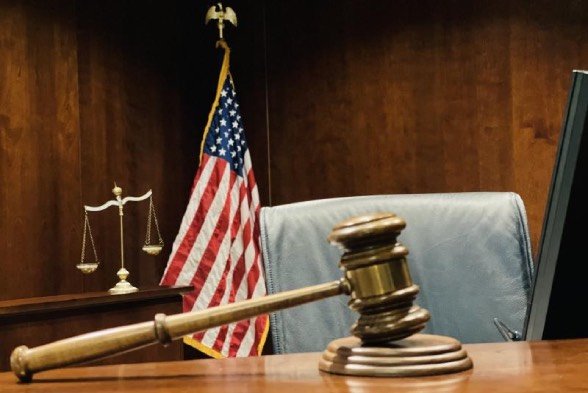A judge's gavel on in a court room in front of a U.S. flag and set of scales