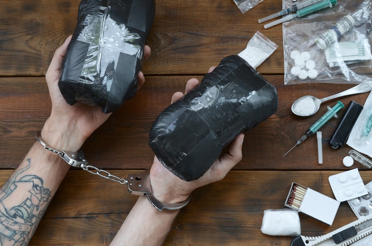 A person in cuffs holding evidence of drug crimes
