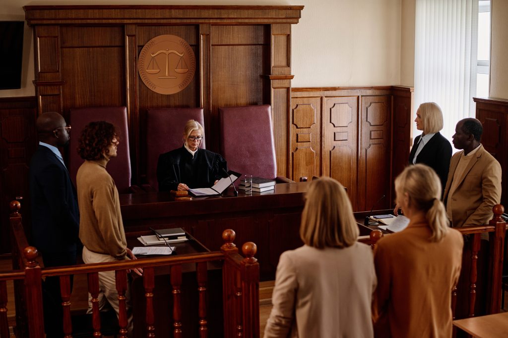 A group of witnesses, attorneys, prosecutor, and suspect standing in a courtroom