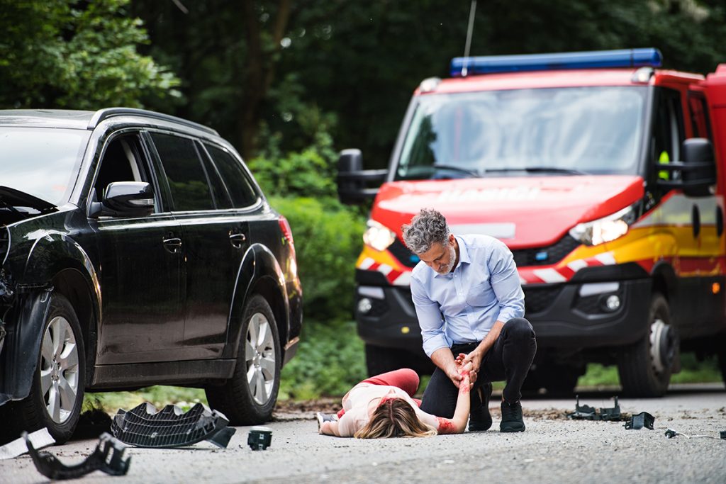 A man helping a young woman lying unconscious on the road after a car accident
