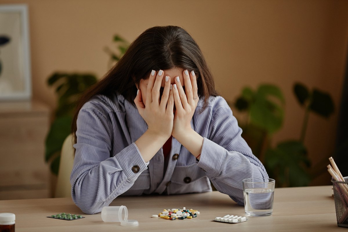 A woman crying over a pile of prescription medications