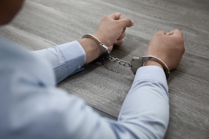 A man in handcuffs with both hands on the desk