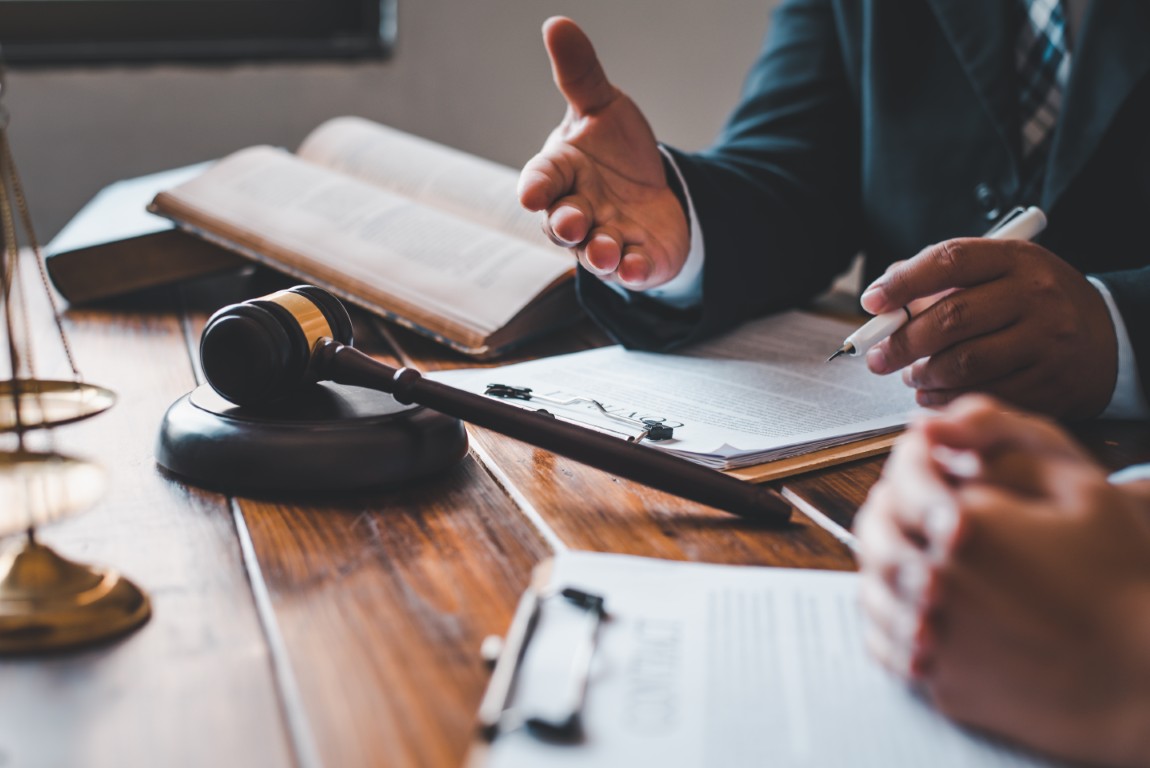 A lawyer sitting next to a client at a table with paperwork and a gavel