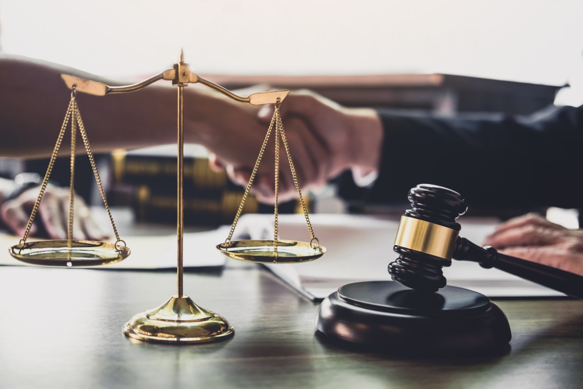 A lawyer shaking hands with a client next to a gavel and set of scales