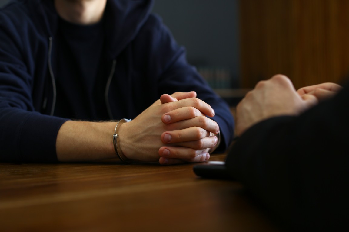 An accused person in handcuffs in an interrogation with a detective